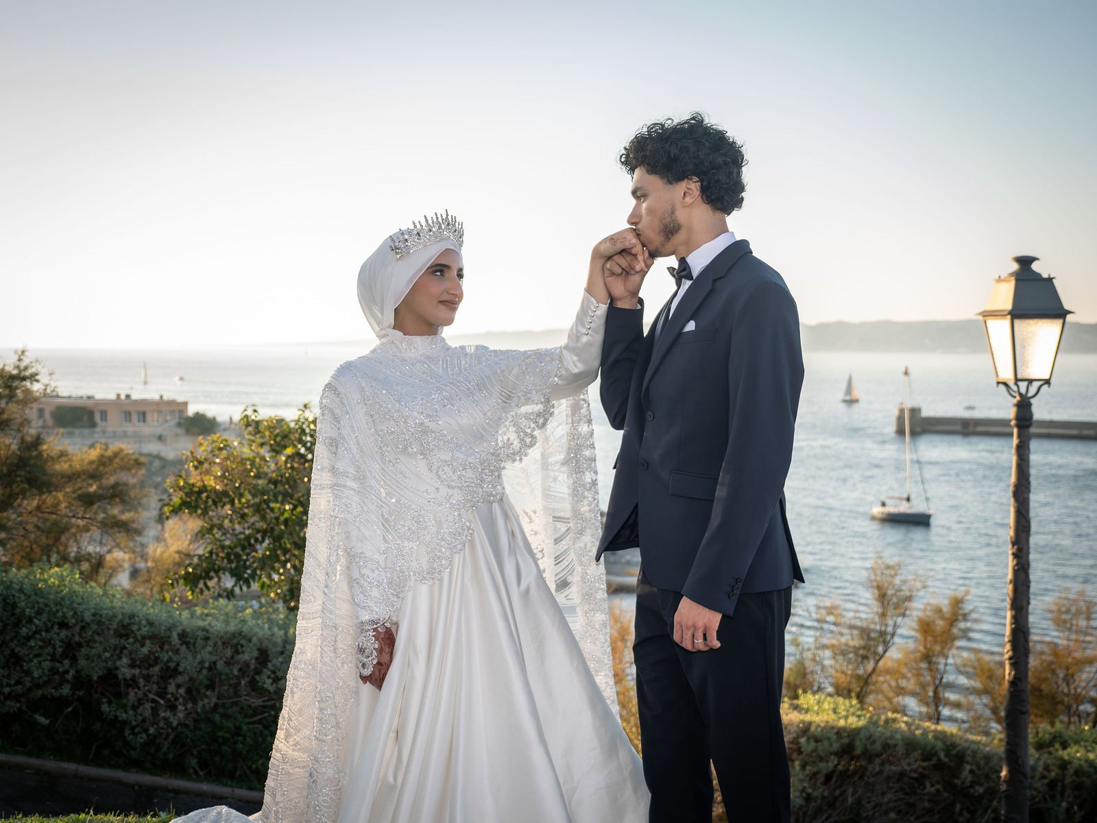 La mariée en couronne embrasse la main du marié face au port
